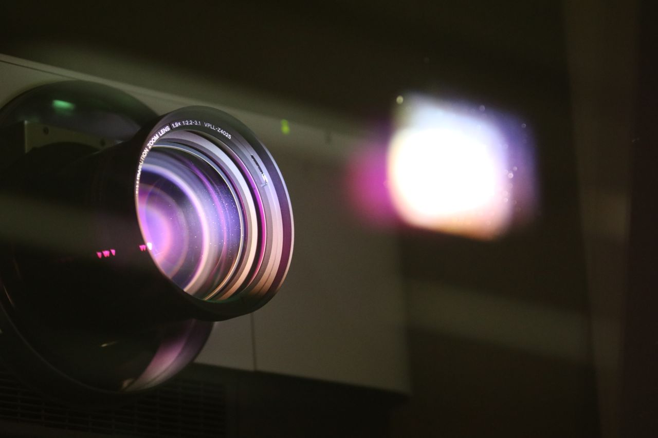 Home Close-up view of a projector lens with light reflections, highlighting optics and technology.