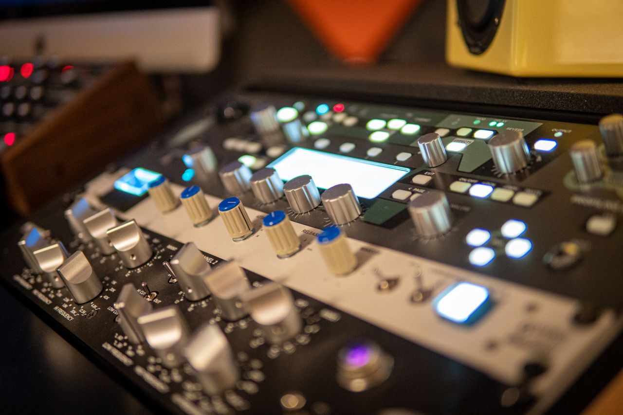 Home Close-up of a professional audio mixer with knobs and lights in a modern recording studio setting.