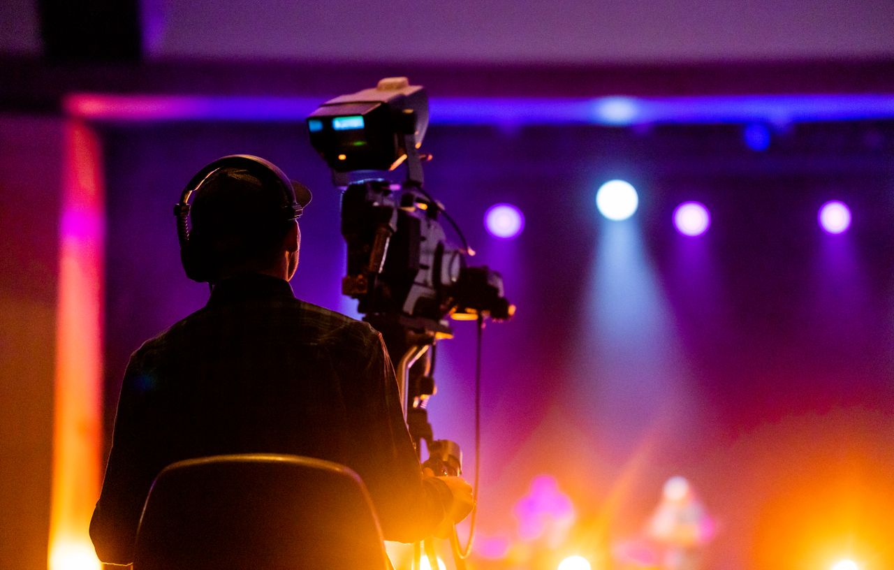Home A videographer recording a live concert with vibrant spotlights, using professional equipment.